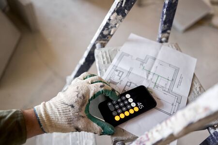 The construction worker calculates the area of the room on the calculator. Architectural blueprints....