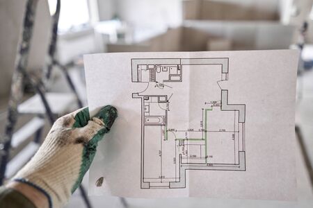 The construction worker hold in hands Architectural blueprints. Repair or construction of a new apartment. Concept for new house design or home improvement. Development of the apartment project.の写真素材