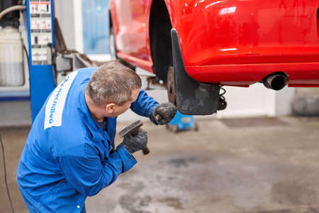 Russia, Nizhny Novgorod - march 13, 2020: Best way Auto service. Auto mechanic changes the brakes on the car. Rusty drum brakes, rear on red car. Change the old to new brake disc on car in a garage.のeditorial素材