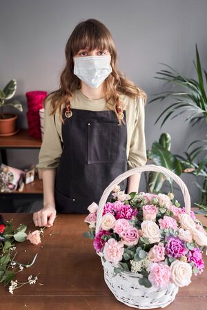 Florist woman in a medical mask for protection from coronavirus. Pandemic concept, working during an epidemic. Small flower shop. Flowers delivery.の写真素材