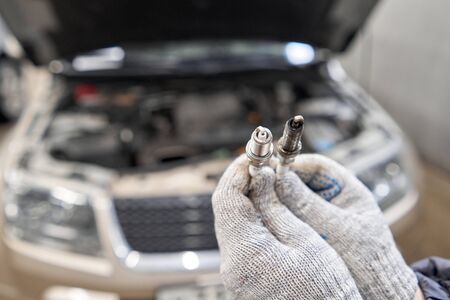 Old and new spark plugs. Comparing spark plugs the maintenance of the engine, on the hands of a mechanic.の写真素材