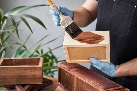 Man carpenter varnishing wooden crate for flowers with brush in her small business woodwork workshop. In your work, do you use stains or wood preservatives to show the wood pattern.の写真素材