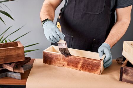 Man carpenter varnishing wooden crate for flowers with brush in her small business woodwork workshop. In your work, do you use stains or wood preservatives to show the wood pattern.の写真素材