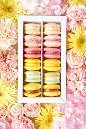 round beautiful sweets macaroni in a festive box with flowers on a flowers background. Still life with macaroni cakes and different flower.の写真素材