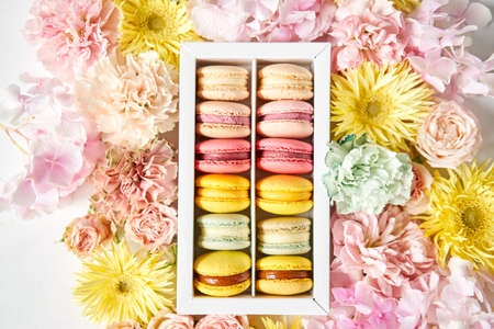 round beautiful sweets macaroni in a festive box with flowers on a flowers background. Still life with macaroni cakes and different flower.の写真素材