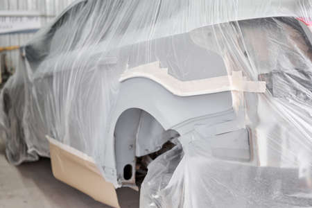 Garage painting car service. section of the car is covered with primer. vehicle is covered with protective paper. Repairing car body work after the accident by working sanding primer before painting.の写真素材