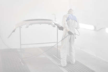 All in a haze of paint. Worker painting parts of the car in special painting chamber, wearing costume and protective gear. Car service station.の写真素材