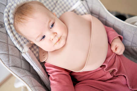 Portrait of a baby with dirty lips. Young mother feeding her baby daughter with fruit puree. The baby is 7 months old, lying in a special high chair for babies.の写真素材