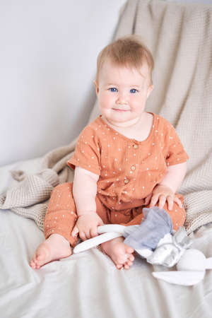 Portrait of a cute 9 months old baby girl seating on a bed. playing with a bunny toyの写真素材