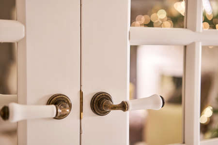 Beautiful modern door knob. Christmas lights on the background. Open, wooden front door from the interior of an upscale home with windows.の写真素材