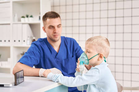 A pediatrician diagnoses lung disease and provides treatment. Breathe the medicine through a nebulizer inhaler.. Portrait of adorable little boy visiting doctor.の写真素材