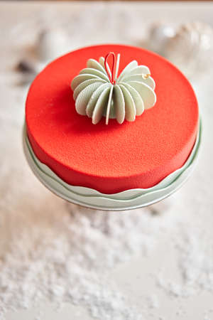 Mousse cake covered with red velour. Dessert on a snow-covered table. Modern european cake. French cuisine. Christmas theme. Copy spaceの写真素材