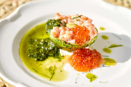 Raw salmon tartare. Fresh salmon, avocado and pesto sauce with red caviar on a plate. Selective focusの写真素材