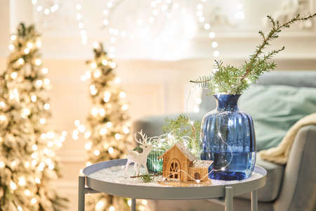 Decorated table in the Christmas interior. Christmas tree. Close-up a small house, Cones, garland,...