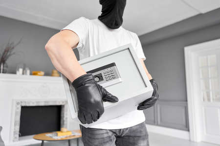 Thief with black mask stealing modern Metal safe with an electronic lock. Home theft of money and documents concept.の写真素材