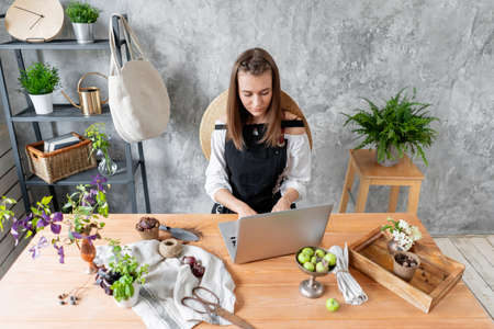 Young female freelancer works on a laptop, responds to messages in social networks. Flower delivery concept. Professional worker in a flower shop.の写真素材