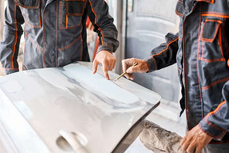Two workers discuss the execution of the work of Repairing car body, Application putty close up. The mechanic repair the car. Work after the accident by working sanding primer before painting.の写真素材
