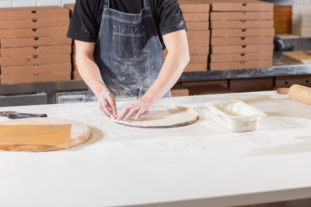 Dough for pizza, the chef rolls out the blanks. Closeup hand of chef baker in uniform white apron...