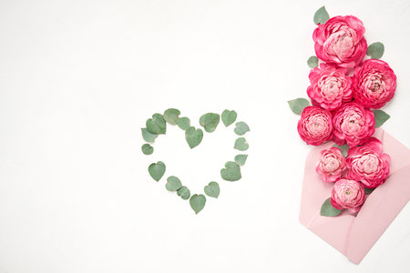 Love letter. white card with pink paper envelope mock up. Petals of flowers, roses and ranunculus. Valentines day romantic background . Space for text.の写真素材