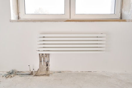 connection heating pipes to white Radiator in a new apartment under construction. Work As A Plumber, mounting water heating radiator on the white wall indoorsの写真素材