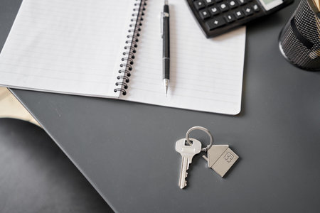 Key with house shaped keychain on table . Modern light apartment interior. Mortgage concept. Real estate, moving home or relating property.の写真素材