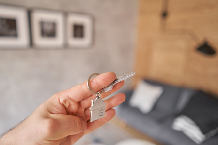 Men hand holding key with house shaped keychain. Modern light lobby interior. Mortgage concept. Real...