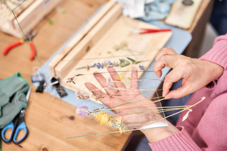 A woman lays out a composition. Master class on creating frame with Herbarium in tiffany technique in stained glass. Herbarium of dried different plants and flowers placed under a glassの写真素材