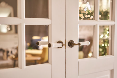 Beautiful modern door knob. Christmas lights on the background. Open, wooden front door from the...