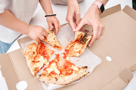 Mother and daughter had a pizza picnic in the park. Pizza delivery concept in a cardboard box. Baked a delicious pizza Margarita in a traditional wood-burning oven in a Neapolitan restaurant, Italy.の写真素材