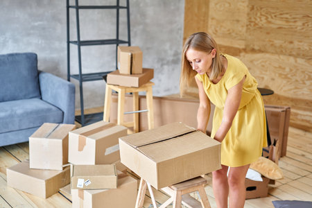 Young girl packing plates into the boxes ready to move. Woman unpacking moving boxes in her new...
