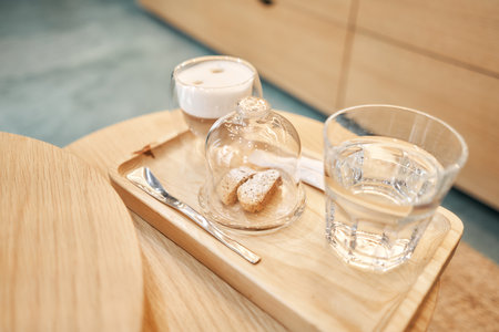Cup of coffee cappuccino with cantuccini and a glass of water on a wooden tray. Coffee with milk, a cookie and a glass with water on a glass table.の写真素材