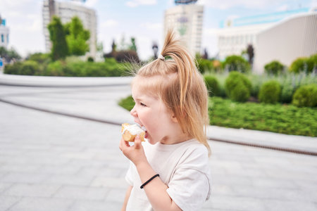 A hungry child enjoys eating ice cream outdoors. Portrait of a cute baby licking a creamy ice cream while walking in a city park, outdoor activities.の写真素材