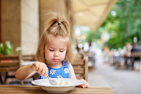 Little kid having breakfast at cafe. Adorable girl drinking still water, eating rice porridge with mango. enjoying breakfast.の写真素材