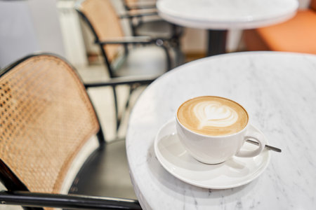 A cup of hot cappuccino on the table in the coworking space of the coffee shop. A cup of coffee on the veranda on a sunny day. Coffee break at the cafe. Close-upの写真素材