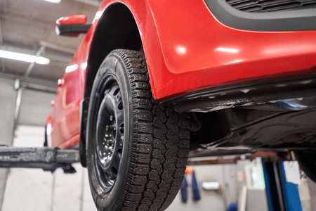Red car on an elevator or hoist in a repair workshop or garage with focus to wheel. Automobile...