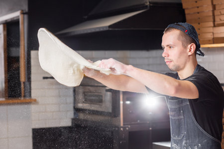 Dough for pizza, the chef rolls out the blanks. Closeup hand of chef baker in uniform white apron...