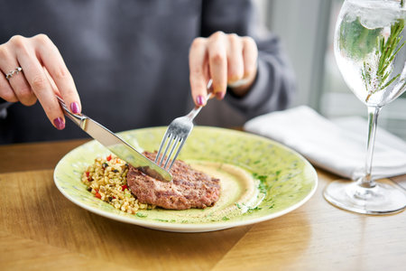 Lunch in a restaurant, a woman cuts delicious Beefsteak marbled beef, served with bulgur and smoked onion cream. Barbecue restaurant menu, a series of photos of different meatsの写真素材