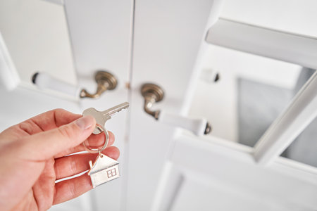 Men hand holding key with house shaped keychain. Modern light lobby interior. Mortgage concept. Real...