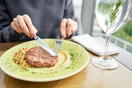 Lunch in a restaurant, a woman cuts delicious Beefsteak marbled beef, served with bulgur and smoked...