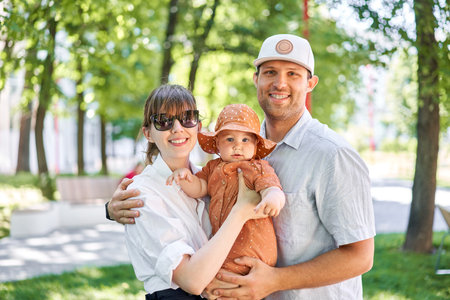 Portraits happy family. Young mother, father and their daughter of acute 10 months old baby girl. Walking on the playground, on a sunny summer day.の写真素材