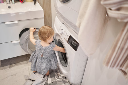 House cleaning and change of bed linen. Happy baby girl one and a half, helper are having fun and smiling while in a bright apartment. Helps parents change bed linen and do laundry in the washing machine.の写真素材