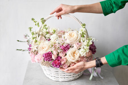 Flower arrangement in Wicker basket. Beautiful bouquet of mixed flowers in woman hand. Handsome fresh bouquet. Small flower shop and Flowers deliveryの写真素材