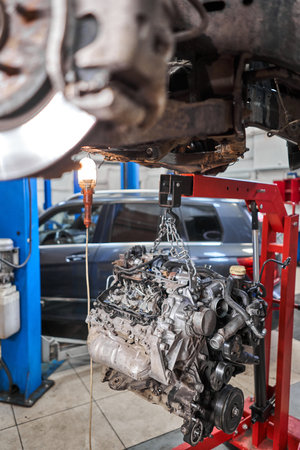 A car mechanic inspects the engine with a flashlight. Engine Block on a repair stand with Special crane jack. Technical service station for car.の写真素材