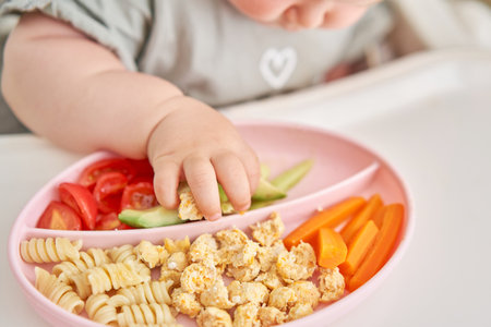 Cute child eats healthy food pasta and vegetables steamed,. Portraits of a cute 10 months old baby girl. The baby sitting in a special high chair for babies.の写真素材