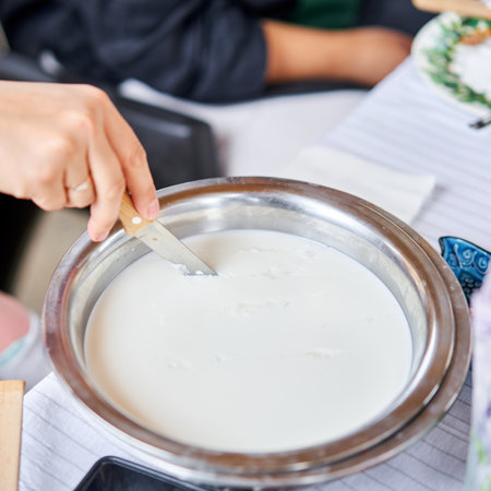Cut with a knife, separate the serum. Master class and cheese tasting. Women make cheese. The enzyme and starter culture are added to the milk in a metal container. Milk folding process, home production, business, entrepreneur.の写真素材