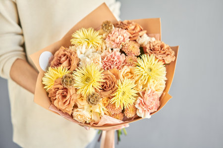 a beautiful bouquet of fresh flowers in the hands of a florist. A gift bouquet in a peach color scheme for any holiday. A very nice female florist is holding a beautiful colorful bouquet of fresh flowers on a gray wall backgroundの写真素材