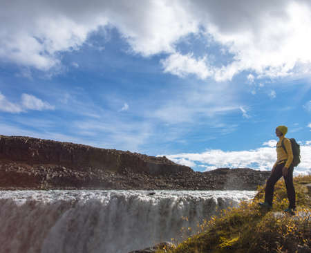 The famous Icelandic giant Dettifoss waterfall and a woman dressed in yellow in the foreground.の写真素材