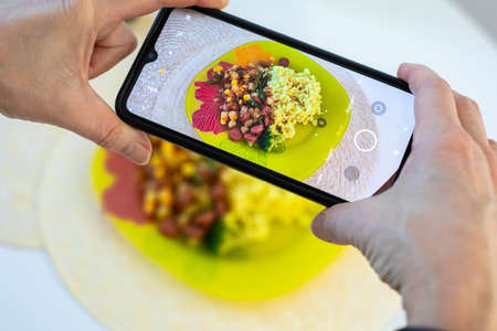 Photographing food on a smartphone. Yellow plate with rice and vegetables. Healthy natural foodの写真素材