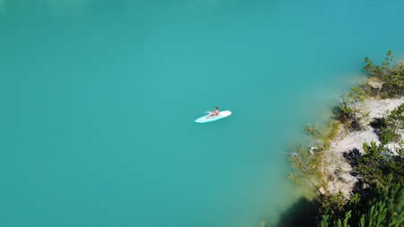 A girl in a dress floats on a glanders board on a pond with bright turquoise water. Warm summer day for travel. Top view from a quadcopter. Aerial photographyの写真素材