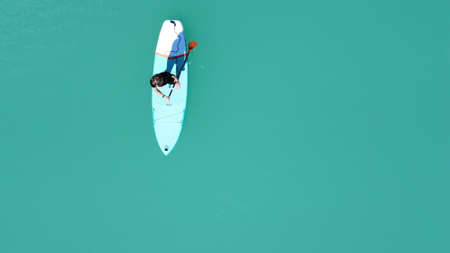 A girl in a dress floats on a glanders board on a pond with bright turquoise water. Warm summer day for travel. Top view from a quadcopter. Aerial photographyの写真素材